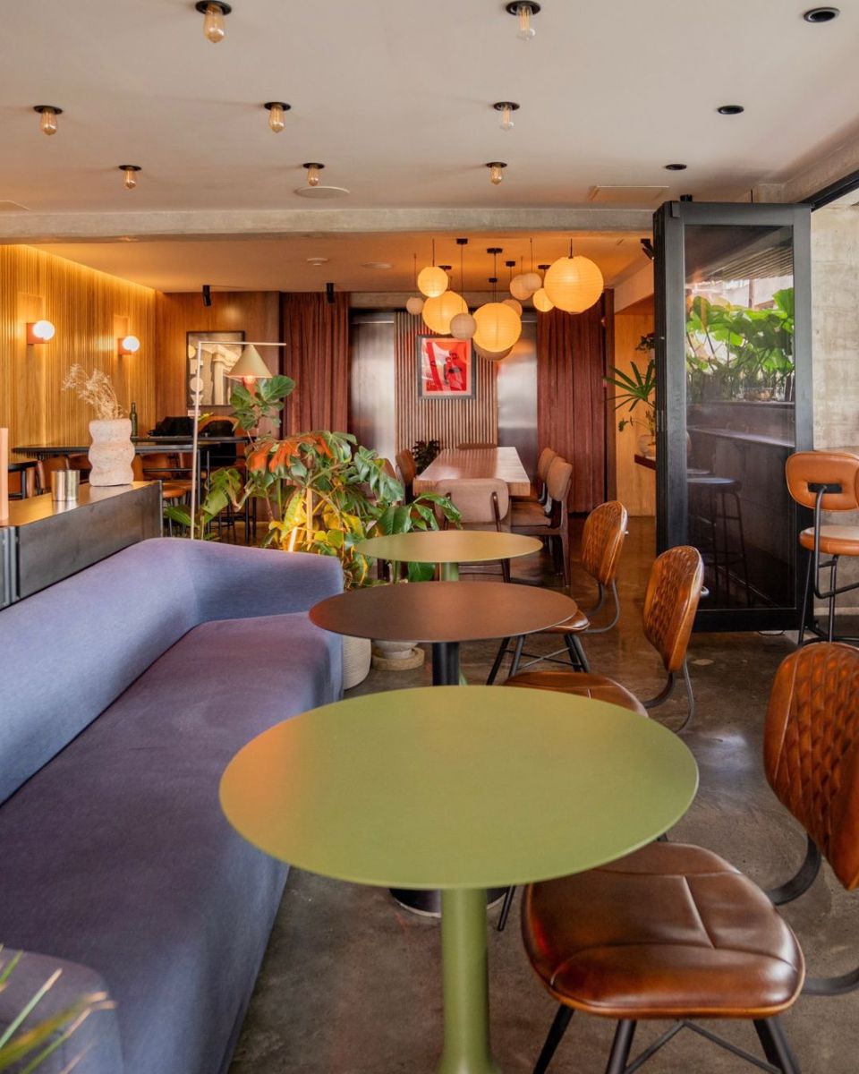 Sofá, mesas verdes y barra de café en el salón de Bacán
